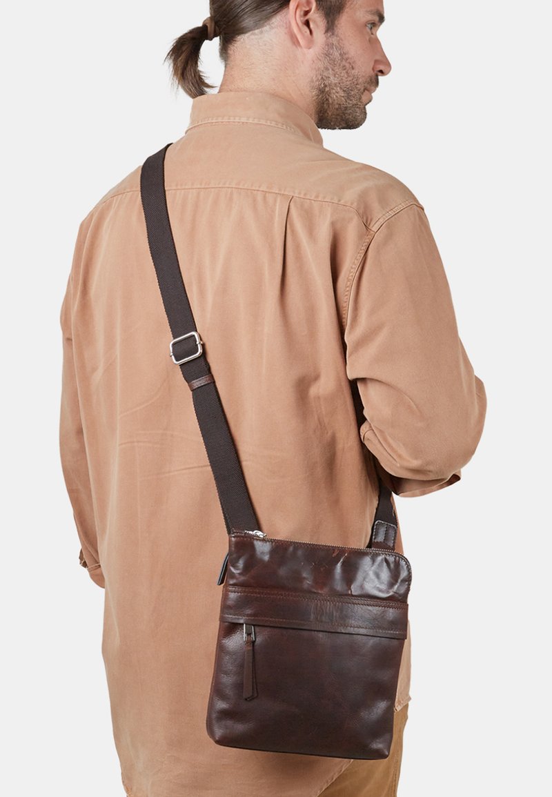 Hnědá kožená crossbody taška s hladkým povrchem, zipovým uzávěrem a nastavitelným textilním popruhem. Kompaktní obdélníkový tvar; detail přední kapsy.