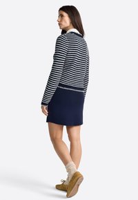 Cardigan a righe blu navy sopra una gonna blu navy, abbinato a calzature gialle e calze color crema. Il cardigan presenta una texture a costine.