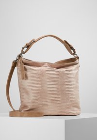 Borsa beige in pelle texturizzata con manico corto e tracolla lunga staccabile, poggiata su una superficie bianca contro uno sfondo grigio.