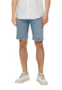 Shorts de mezclilla azul claro con corte recto, dobladillo deshilachado, combinados con una camisa blanca con estampado y zapatillas de color claro.