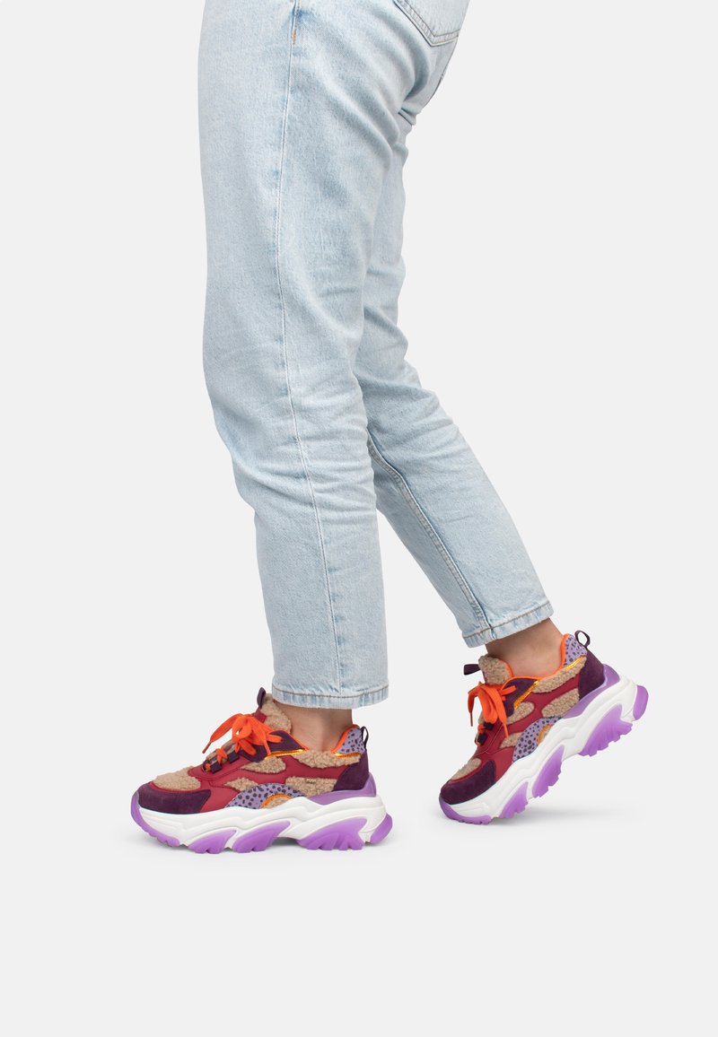 Zapatillas deportivas multicolores con acentos en púrpura, naranja y marrón. Suela gruesa blanca con patrones texturizados y cordones. Diseño casual.