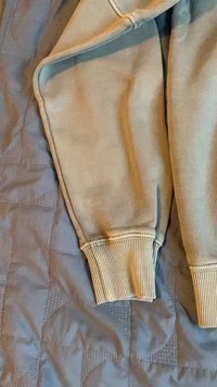 Világosszürke pulóverujj ribbed mandzsettával. Az anyag lágy és enyhén textúrált, finom színváltozatokkal és varrási részletekkel.