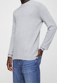 Gray ribbed long-sleeve shirt with a crew neckline. The fabric appears textured and lightweight. Worn with blue jeans.