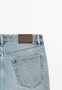 Tył jasnoniebieskich dżinsów pokazujący tylną kieszeń oraz brązową skórzaną metkę marki "Massimo Dutti" na pasie.