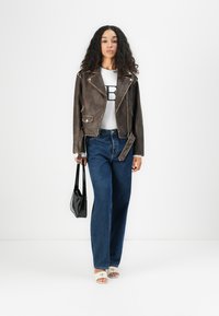 Brun kunstskinn bikerjakke med sølvdetaljer, hvit T-skjorte med logo, høydejusterte blåjeans og svart håndveske.