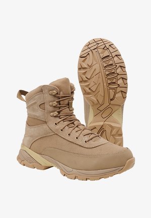 Stivali tattici beige con una combinazione di pelle scamosciata e materiale in rete, caratterizzati da un design alto alla caviglia, cinque coppie di occhielli e una suola in gomma texturizzata.