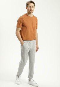 Koszulka z krótkim rękawem w rdzawym odcieniu, połączona z szarymi spodniami dresowymi. Mieszanka bawełny, luźny krój, elastyczny pas i boczne kieszenie. Białe trampki.