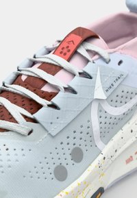Sneakers da trail Nike con una parte superiore in rete blu chiaro, accenti testurizzati rossi e rosa, lacci bianchi e una suola intermedia bianca macchiata.