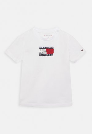 Wit T-shirt met korte mouwen en een rechthoekig Tommy Hilfiger-logo in zwart, wit en rood, gecentreerd op de borst.