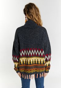 Prevelik temno siv pulover s pisanimi geometrijskimi vzorci v rdeči, rumeni in beli barvi. Ima resaste robove in široke rokave.