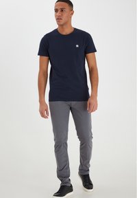Marinblå bomulls t-shirt med en liten logotyp på bröstet, i kombination med grå slim-fit byxor och svarta sneakers med vit sula.