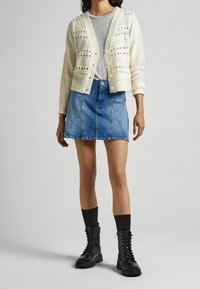 Stickad krämfärgad cardigan med mönster, grå t-shirt, denim mini kjol och svarta kängor med snörning och tjock sula.