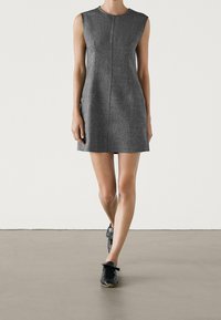 Robe grise sans manches à coupe droite, avec des coutures verticales et un design minimaliste, associée à des chaussures de sport noires.