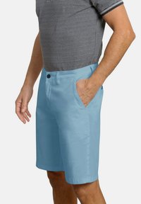 Pantalones cortos de color azul claro, hechos de un tejido suave, con bolsillos laterales y cierre de botón, combinados con una camisa de patrón en blanco y negro.