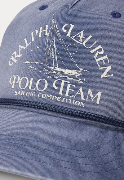 Sinine pesapallimüts valge tekstiga "Ralph Lauren Polo Team Sailing Competition" ja purjelaevagraafikuga äärest üleval.