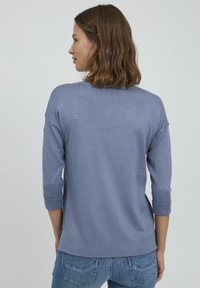 Helles blauer Strickpullover mit Dreiviertelärmeln, gerippten Bündchen und geradem Saum, getragen mit blauen Denim-Jeans.