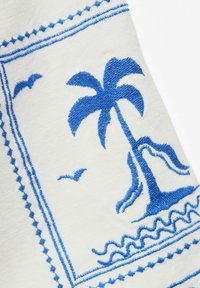 Palmier bleu brodé, oiseaux et vagues de l'océan sur tissu blanc avec couture décorative bleue en bordure.