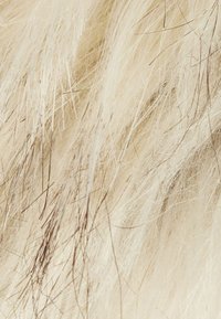 Tissu en fausse fourrure crème, avec de longues fibres douces et de subtiles rayures marron foncé, créant une apparence texturée et superposée.