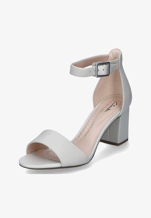 Weiße Kunstleder-Absatzsandalen mit offenem Zeh und Knöchelriemen, ausgestattet mit einer quadratischen Schnalle und einem Blockabsatz für Stabilität.