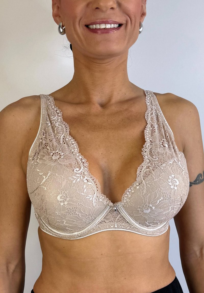 Sujetador de encaje beige con patrones florales, diseño de escote en V profundo y aros suaves; tirantes de encaje transparente con bordes en forma de onda.