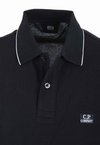 Polo shirt nera realizzata in tessuto testurizzato con colletto, patta a tre bottoni e bordi bianchi. Presenta il logo C.P. Company sul lato sinistro del petto.