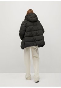 Chaqueta acolchada negra con capucha, diseño acolchado y puños elásticos, combinada con pantalones de pierna ancha color blanco roto.