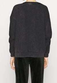 Sudadera de color gris oscuro con un corte relajado, cuello y puños acanalados, tejido texturizado y un aspecto ligeramente desgastado. Se muestra la vista trasera.