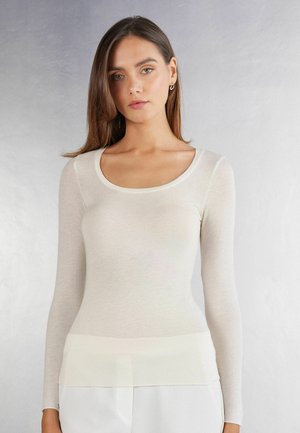 T-shirt ajusté à manches longues en tissu crémeux transparent avec un col rond et une texture lisse. Accentué par un ourlet légèrement plus foncé.