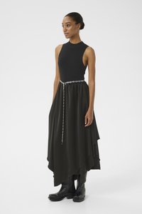 Un haut sans manches noir associé à une jupe asymétrique noire fluide, cintrée avec une ceinture en chaîne argentée, et des bottines noires.