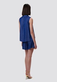 Blusa senza maniche in denim con una vestibilità morbida, abbinata a pantaloni corti coordinati. Il colore è blu scuro e il tessuto presenta una leggera texture.