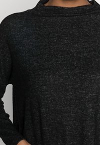 Svart tröja med texturstickning, avslappnad passform och hög krage. Långa ärmar och inga synliga logotyper. Mjuk kvalitet med subtila variationer.