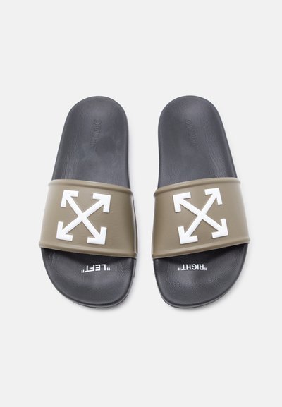 Ζευγάρι μαύρων σαγιονάρων slide με ελαιώδη λουριά που φέρουν λευκά σταυρωμένα βέλη και κείμενο "ΑΡΙΣΤΕΡΟ" και "ΔΕΞΙ" στα πέλματα.