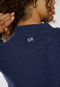 Maglione blu navy con una finitura in maglia testurizzata, caratterizzato da un piccolo dettaglio ricamato "S/B" sul retro del colletto.