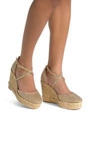 Wedge sandals with a woven jute sole, featuring a metallic accented upper with rhinestones and crisscross ankle strap. Color: gold.