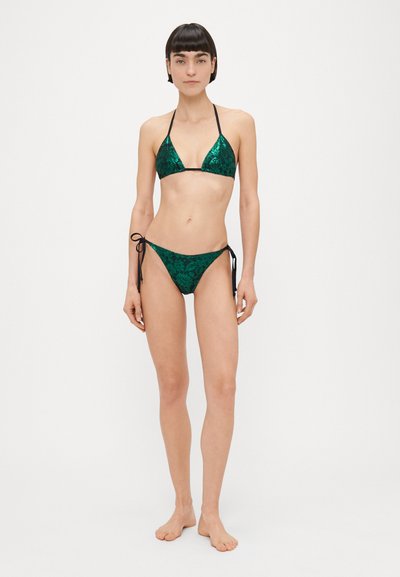 Žalios spalvos bikini kostiumėlis iš žėrinčių sequinių turi trikampio formos viršų su plonomis juodomis petnešėlėmis ir derančias kelnaites su šoninėmis raištelėmis, sukuriantis elegantišką siluetą.