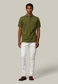 Polokošeľa olivovo zelenej farby s červenými akcentmi, krátkymi rukávmi, zapínaním na gombíky a logom. Kombinovaná s bielymi nohavicami a hnedými mokasínami.