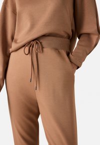 Conjunto de loungewear marrón que presenta una camiseta de corte relajado y pantalones a juego con cintura elástica, cordón y una sutil textura.
