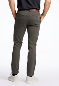 Herrbyxor i olivgrön färg tillverkade av mjukt material, med slim fit, två bakfickor med knappar, och kombineras med vita sneakers.