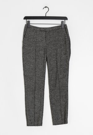 Pantalones de tweed gris ajustados con pliegues marcados y bolsillos laterales colgados en una percha de plástico negro contra un fondo blanco.