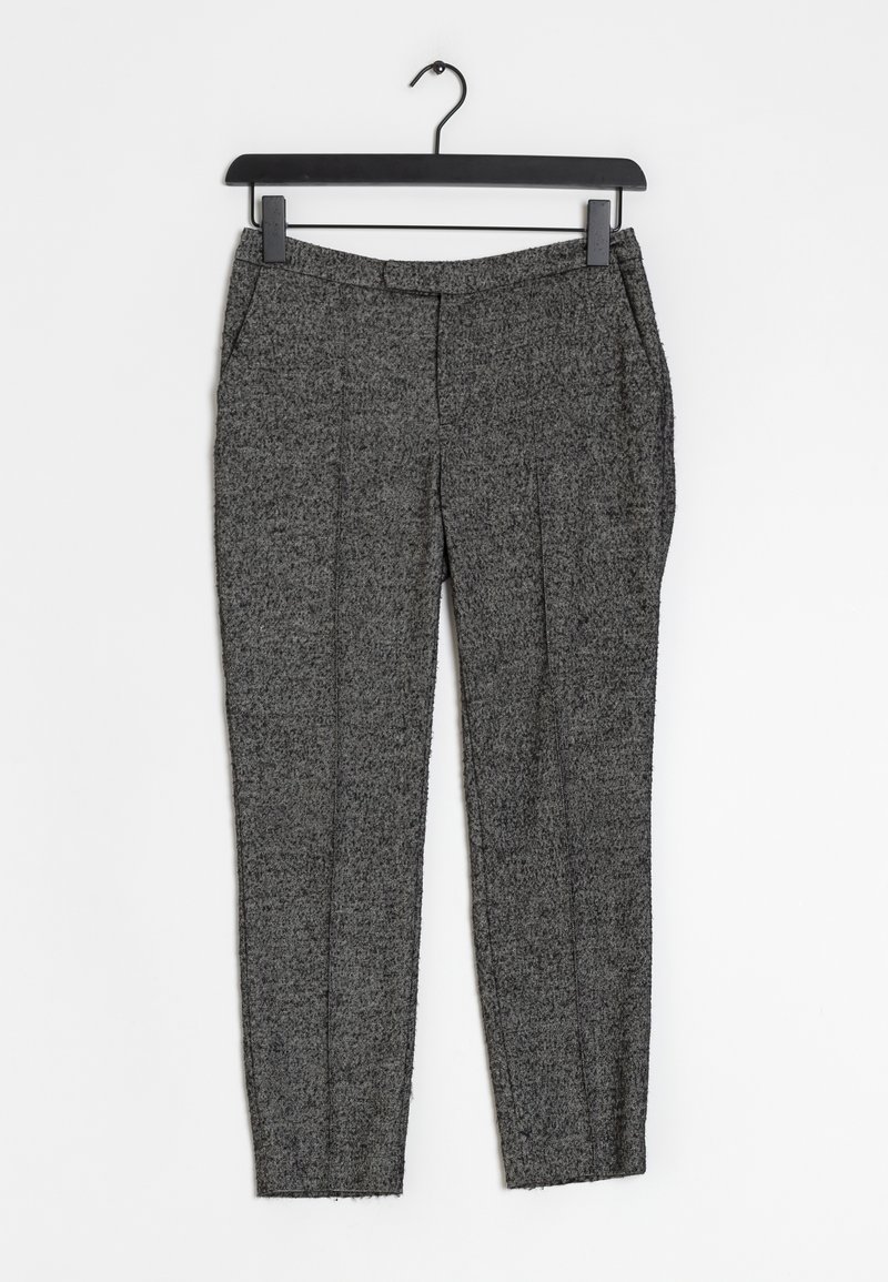 Pantalones de tweed gris ajustados con pliegues marcados y bolsillos laterales colgados en una percha de plástico negro contra un fondo blanco.