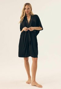 Czarny szlafrok w stylu kimono z szerokimi rękawami, związywany w talii i gładkiego materiału. Posiada głęboki dekolt w kształcie litery V i długość do kolan.