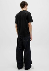 Sort bomulds t-shirt med rund hals og korte ærmer, parret med vidde ben mørk denim jeans. Enkel design, ingen synlige mønstre eller grafik.