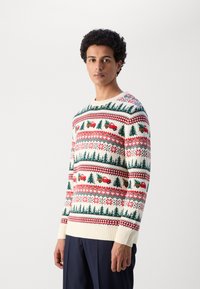Cremefärgad tröja med ett festligt mönster av röda lastbilar, gröna träd och julmotiv. Ribbad mudd och fåll, stickad textur.