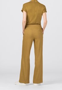 Senapsgul tvådelad outfit med en kortärmad topp och vida byxor. Tillverkad av ett lätt tyg med en mjuk textur.