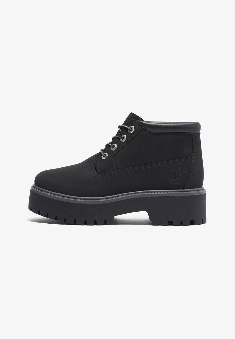 Botte cheville en cuir noir avec semelle à gros crampons, devant à lacets avec œillets métalliques, col rembourré et logo embossé sur le côté.