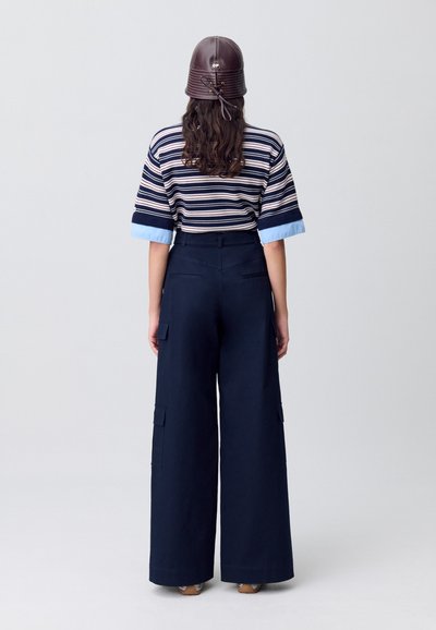 Top de rayas, de manga corta en azul marino y crema, combinado con pantalones amplios en azul marino que cuentan con bolsillos laterales y una textura suave. Sombrero marrón con logo.