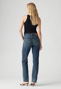 Blugi cu talie înaltă, de culoare albastră, cu picior drept, confecționați din denim. Au două buzunare la spate și o etichetă din piele la talie.