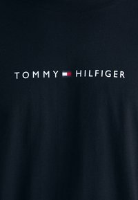 Camiseta de algodón negra con el texto "TOMMY" y "HILFIGER" en blanco, y un pequeño detalle de bandera de color entre las palabras.