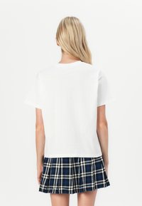 White cotton t-shirt with a relaxed fit, paired with a blue and black plaid pleated skirt. Features short sleeves and a round neckline.