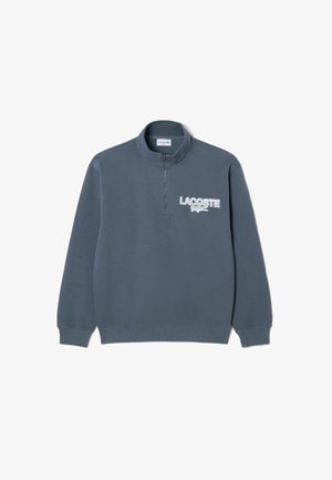 Sweat-shirt gris foncé à fermeture éclair quart, avec poignets et ourlet côtelés, arborant le logo blanc Lacoste et l'emblème crocodile sur la poitrine gauche.